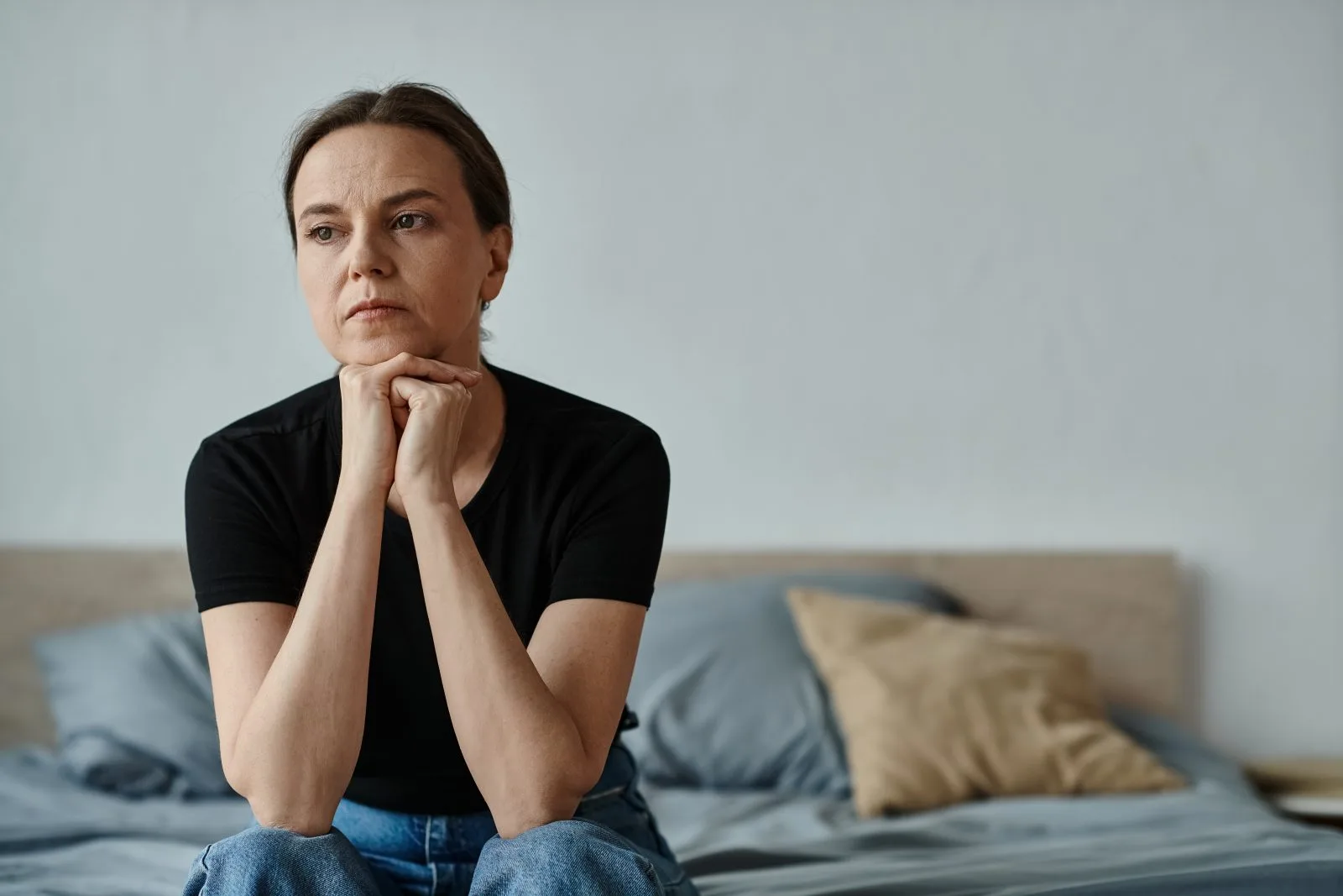 Woman sitting on a bed, deep in thought – online psychiatry in Tacoma, WA